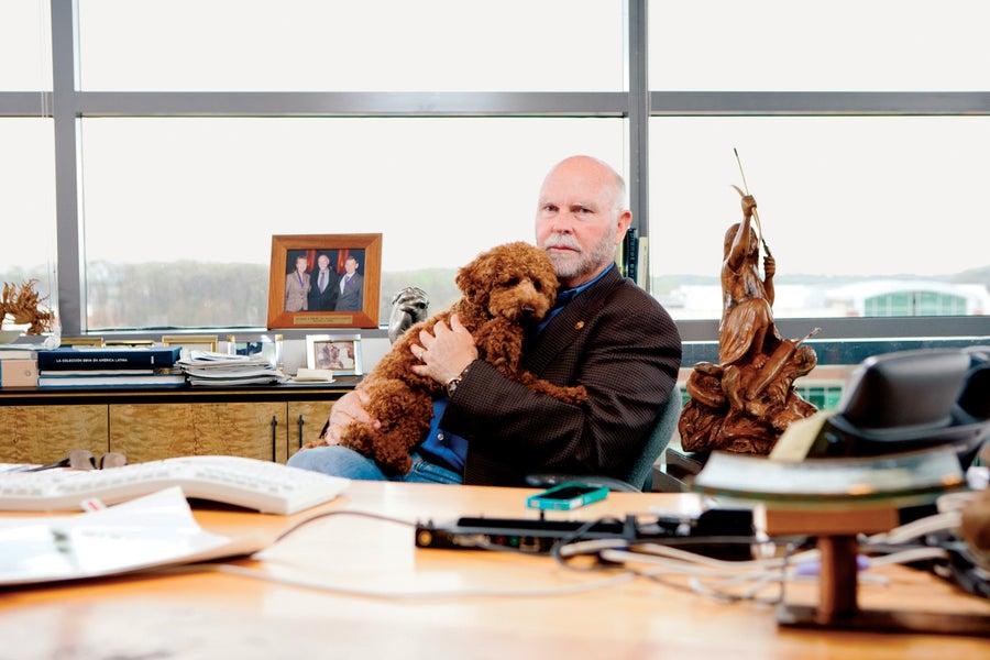 J. Craig Venter sitting at a desk while holding his dog named Darwin. 2011 photograph provided by Eli Meir Kaplan/The Washington Post/Getty Images.