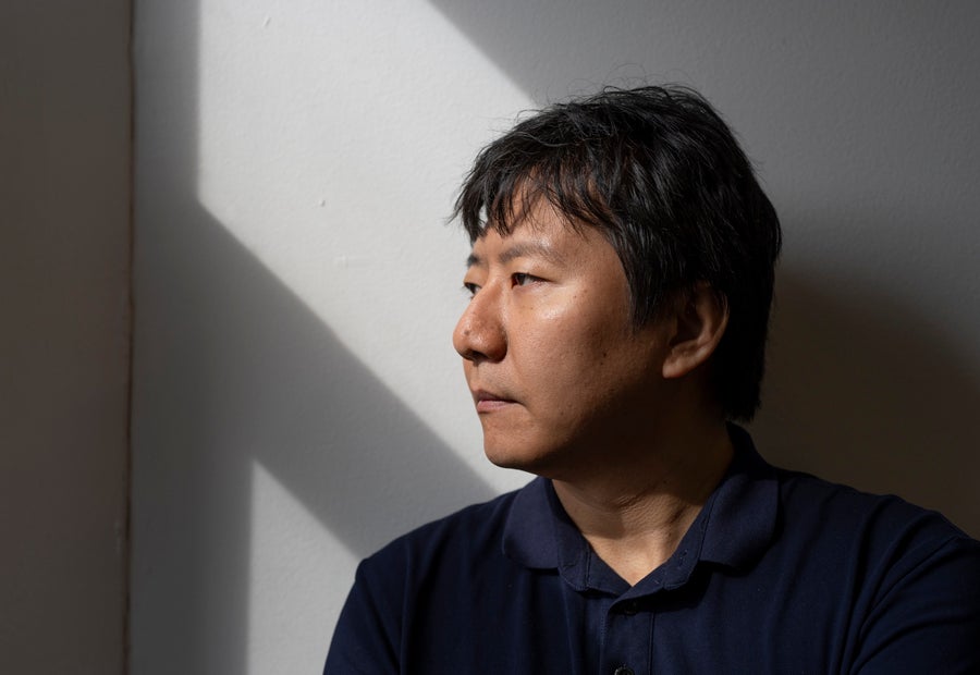 A man looking out a window out of frame, against a sunlit wall.