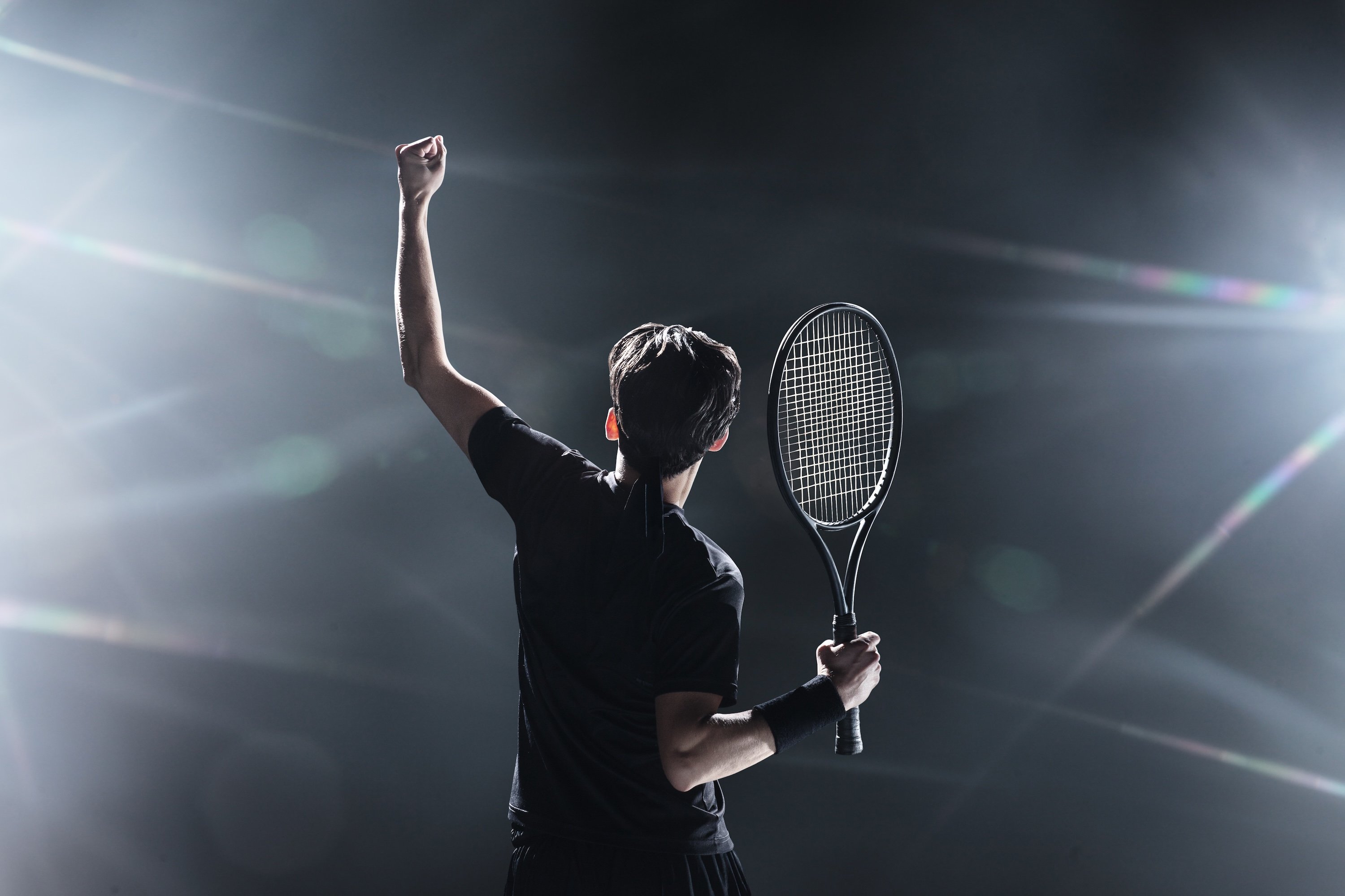 Tennis player raises a fist in victory in front of bright lights.