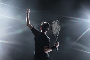 Tennis player raises a fist in victory in front of bright lights.