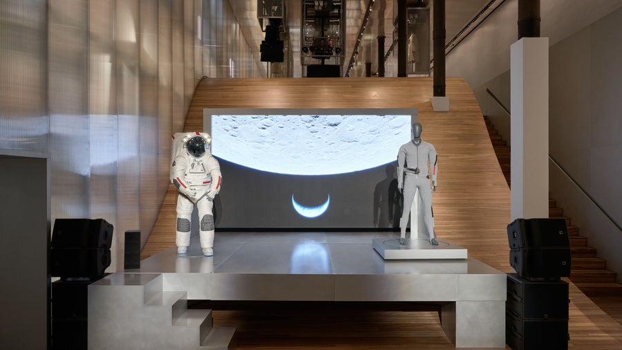 Two space suits next to each other with a photograph of the moon in the background