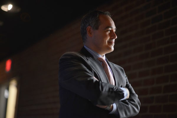 Ángel Cabrera standing in a suit, with his arms crossed, looking to the side.