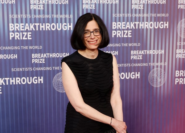 Aviv Regev standing in a black dress against a Breakthrough Prize background.