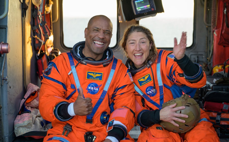 Two astronauts in orange space suits pose gleefully after a safe landing.
