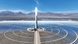 An oblique view from above of a solar panels in a circle around a central tower with mountains and sunny blue skies in the background. Image provided by China News Service/Getty Images.