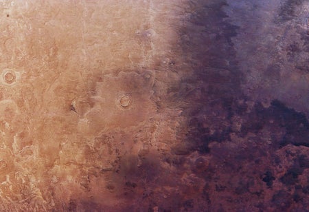 Aerial photo of the rocky, beige-red surface of Mars, with the right half enveloped in shadow.