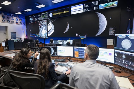 Three scientists in front of several monitiors at Houston Ground Control.