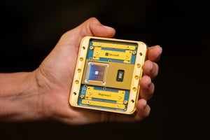 A mostly gold-colored chip with bits of blue showing is held in the palm of a person's hand. The names "Microsoft" and "Majorana 2" are visible.
