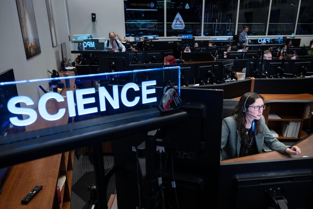 En primer plano, un cartel decía CIENCIA; Al fondo, una mujer sentada en un escritorio en Mission Control.