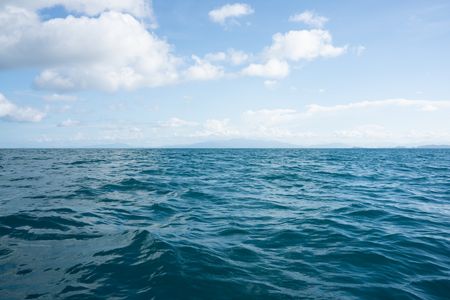 The calm sea on a sunny day with fluffy white clouds and the island scenery in the distance.