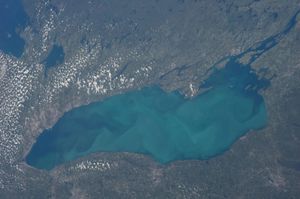 Lake Ontario in various shades of blue, surrounded by brownish land, as seen from above.