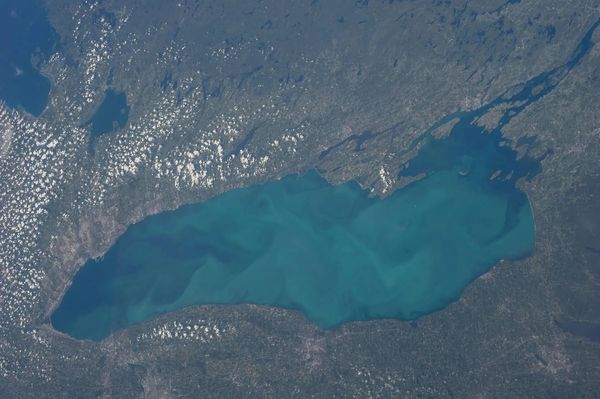 Lake Ontario in various shades of blue, surrounded by brownish land, as seen from above.