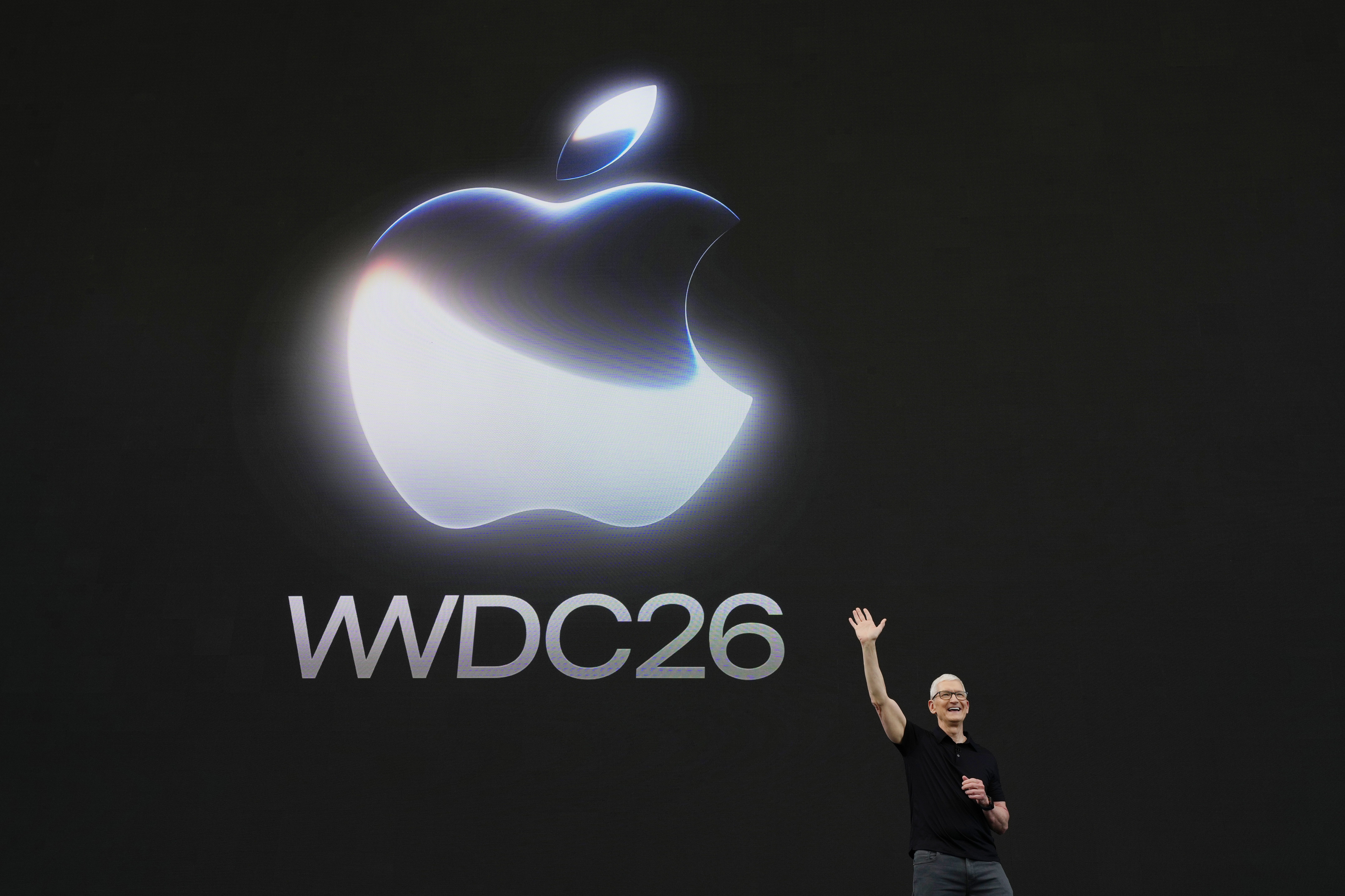A presenter stands on a dark keynote stage below a large glowing logo and conference title.