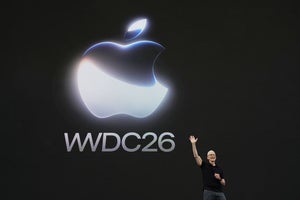 A presenter stands on a dark keynote stage below a large glowing logo and conference title.