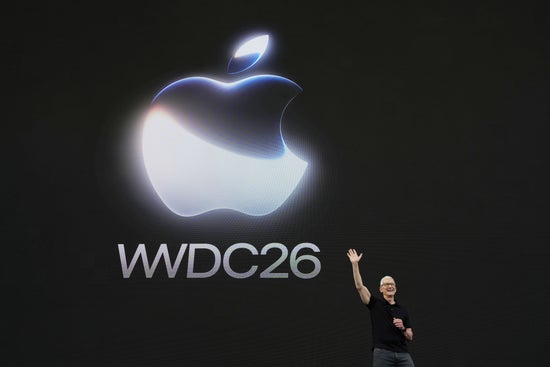 A presenter stands on a dark keynote stage below a large glowing logo and conference title.
