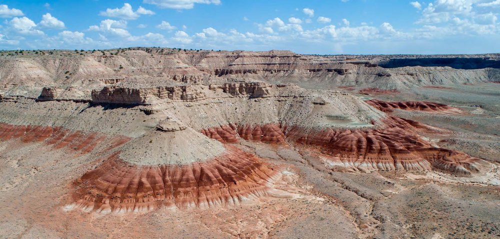 Una vista aérea de una mesa con capas color canela sobre un anillo rojo con un cielo azul con nubes blancas y esponjosas en el fondo