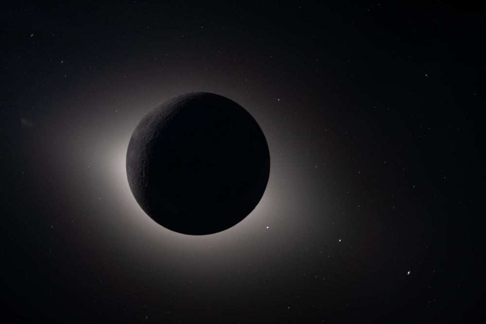 La corona blanca del sol brilla alrededor de la luna, que está casi completamente en sombra. Las estrellas brillan alrededor de la luna.