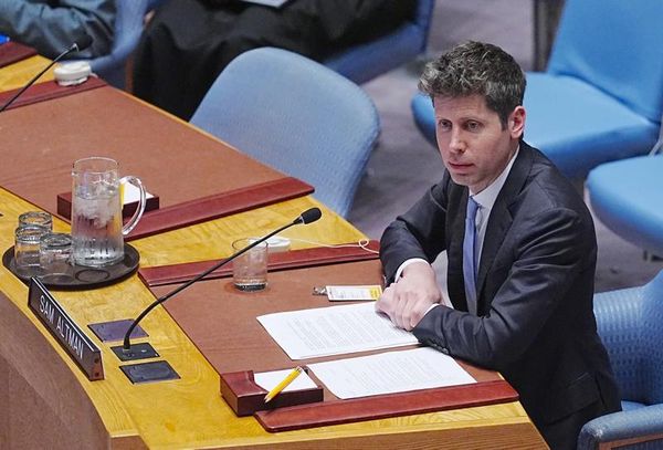 OpenAI CEO Sam Altman sits on a blue chair at a long wooden desk at the United Nations General Assembly.