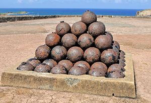 A stack of old looking metal balls with the ocean in the background.