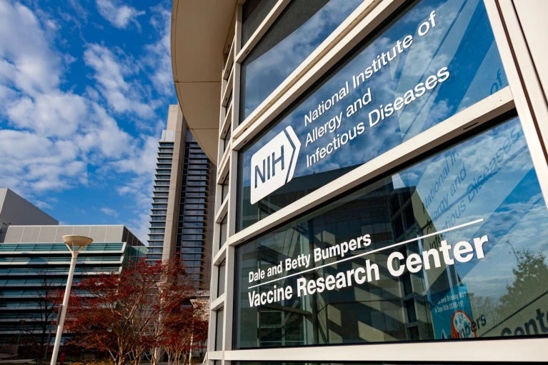 NIH glass building exterior with signage for the National Institute of Allergy and Infectious Diseases and Vaccine Research Center, on a sunny day.