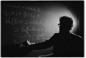 A silhouetted man gestures toward symbolic logic written in chalk across a blackboard.