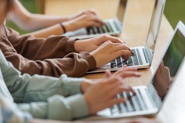 Three teenagers type on laptops