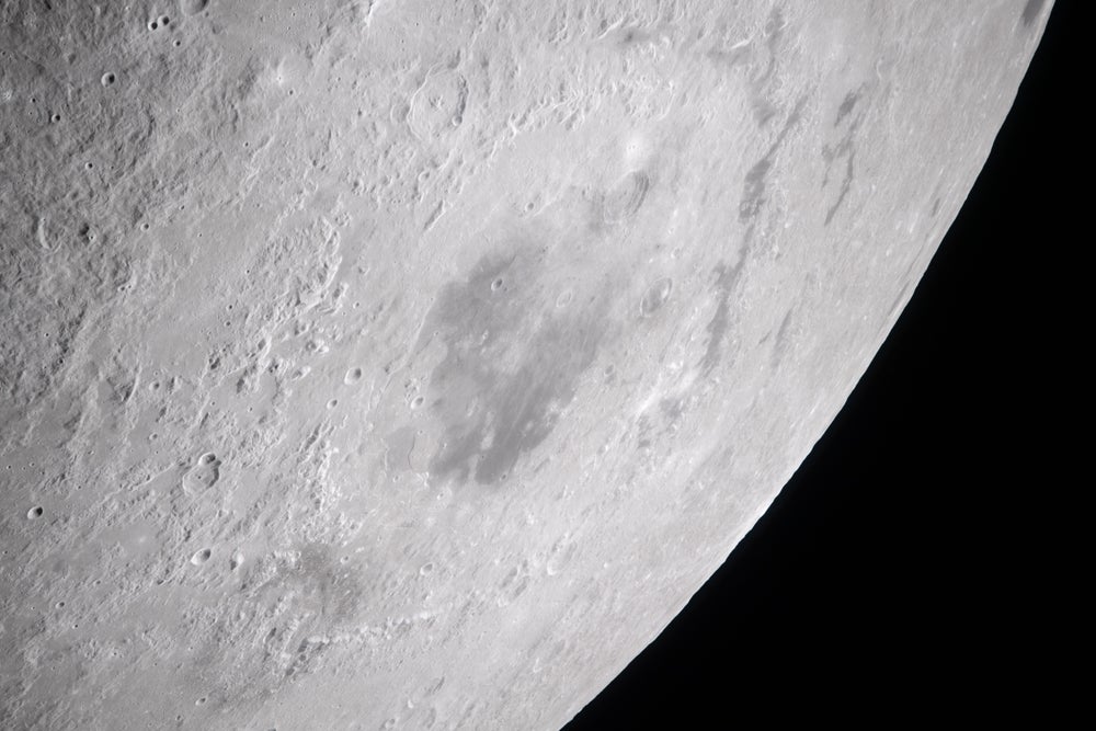 Primer plano de una luna brillantemente iluminada con el espacio visible en la parte inferior derecha y un gran cráter oscuro en el centro del encuadre.