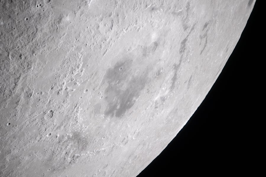 Close-up of brightly lit moon with space visible in bottom right and a large dark crater in the center of the frame.