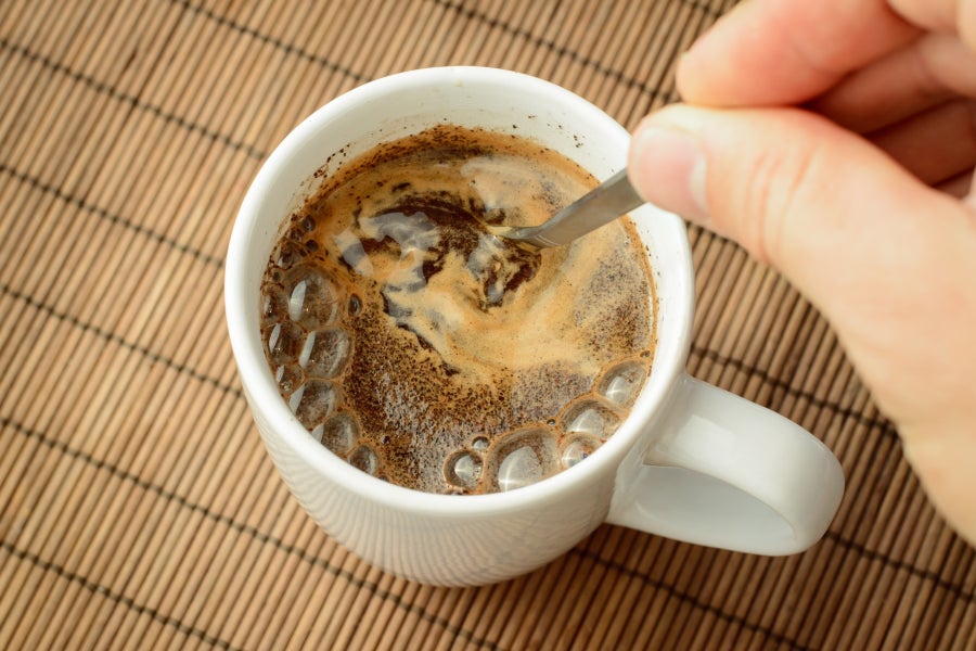 Overhead view of a coffee cup with a hand stirring a spoon through the espresso foam.
