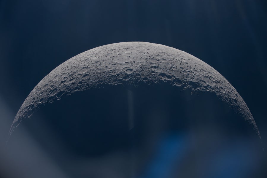 Blurry blue light streaks over a view of half of the moon.