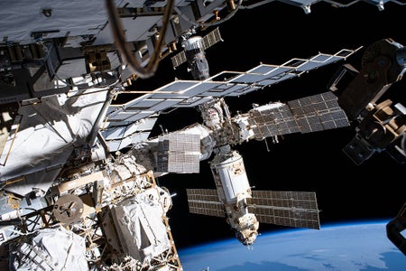 A series of modules and solar panels orbit in space above the curve of Earth’s horizon.