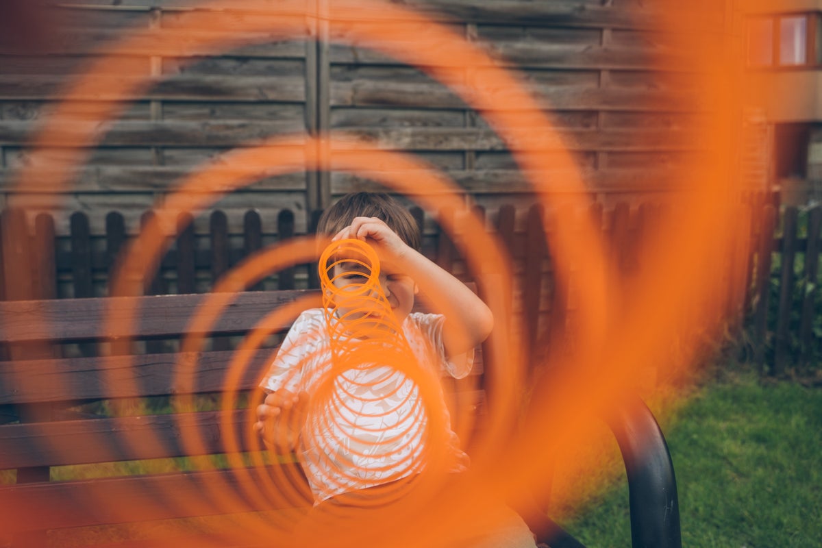 Boy looking through orange spring toy outdoors.