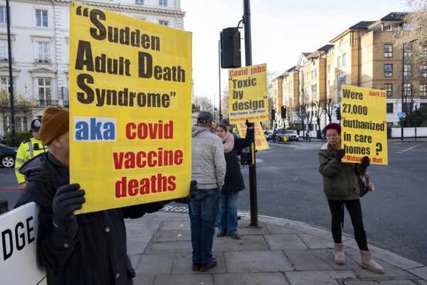 Anti-vax protesters stood on a street corner, holding yellow placards with anti vaccine slogans.