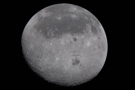 A cratered view of the far side of the moon, separated by a large crater from the smoother surface of the near side visible in the top half the disk.