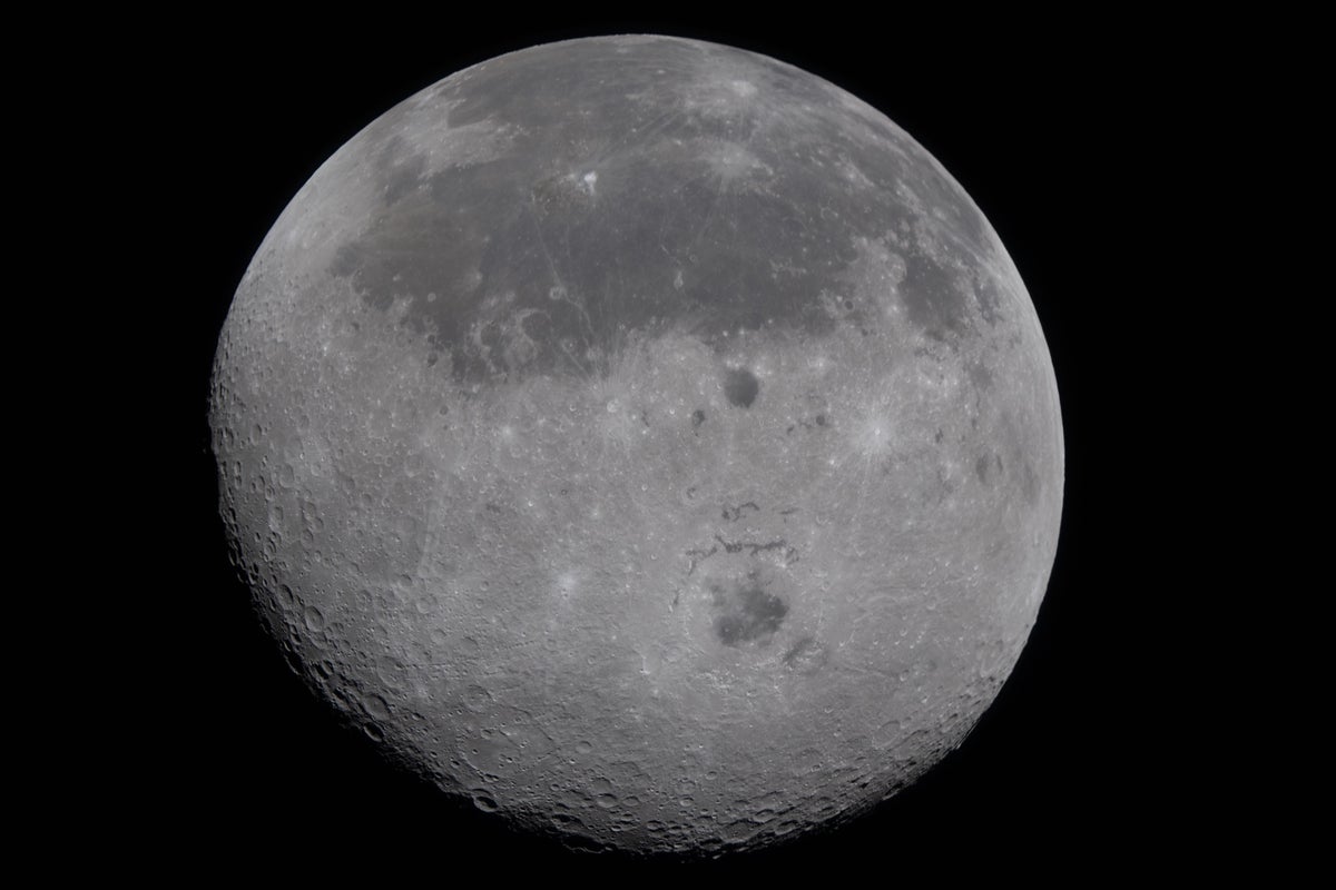 A cratered view of the far side of the moon, separated by a large crater from the smoother surface of the near side visible in the top half the disk.