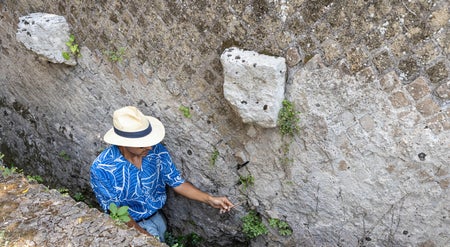 A man in a blue shirt stands in an ancient Roman communal latrine.