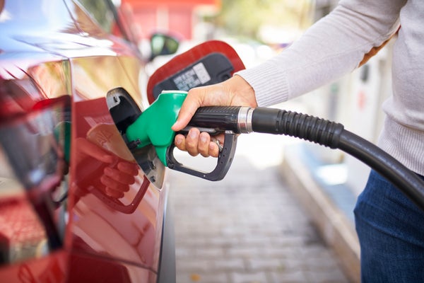 A woman's hand holding a green gas pump filling a red car