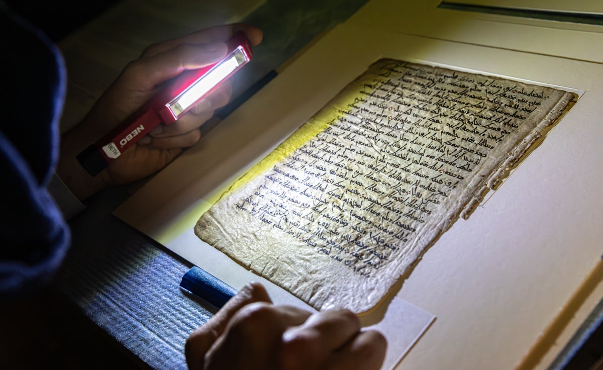 This image shows a researcher holding a red flashlight and shining it on the page of a manuscript.