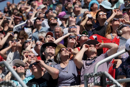 Crowd of people with Eclipse glasses looking up.