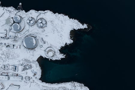 An aerial view with snow-covered buildings on the left and black water on the right