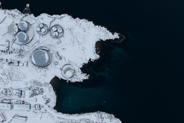 An aerial view with snow-covered buildings on the left and black water on the right