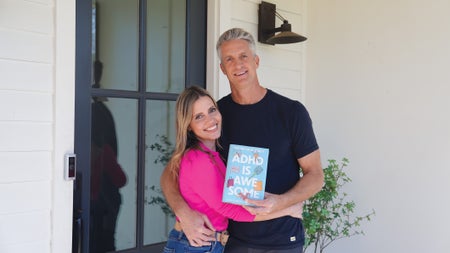 Penn (black T-shirt) and Kim (pink sweater) Holderness side-hugging and holding up their book titled: "ADHD is Awesome."