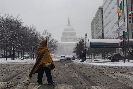 An unhoused person, wrapped with a blanket, walks in the snow and slush covered street near the US Capitol during a snowstorm on January 6, 2025 in Washington, DC