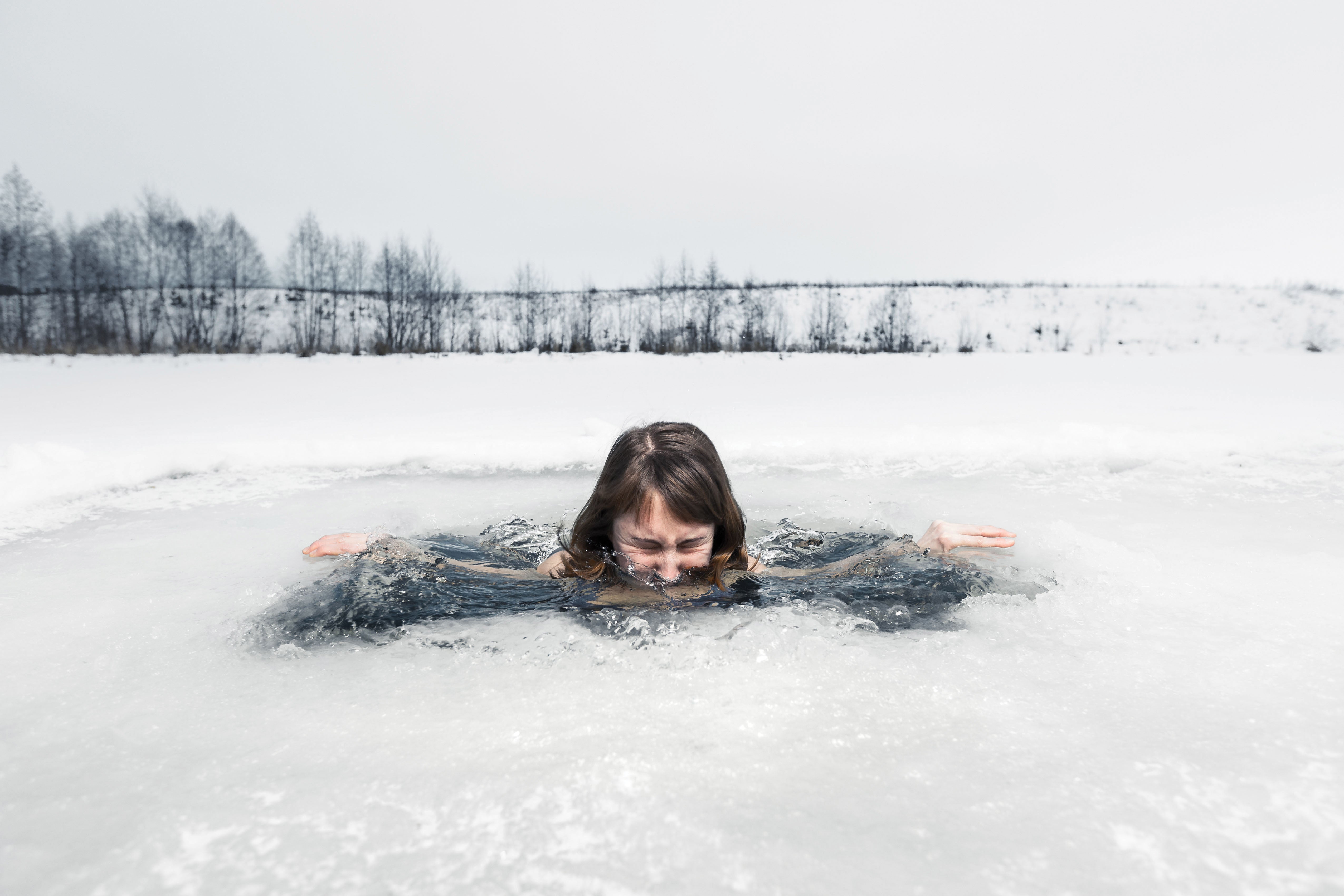 Image of a woman swimming in a frozen lake, with her face half way in the water
