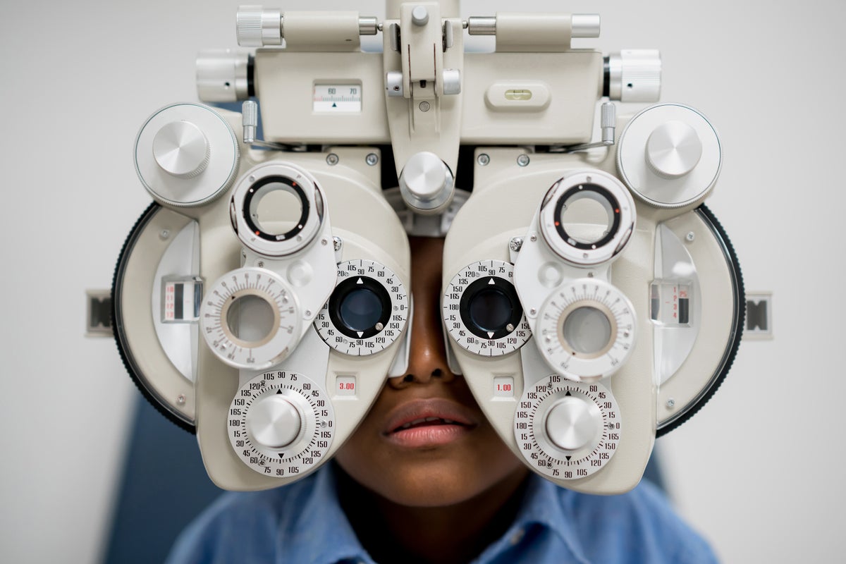 Child looking through a phoropter as part of an eye exam with an optometrist