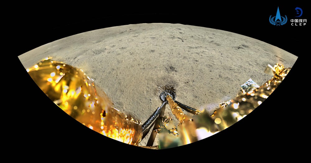 An almond-shaped image against a black background. Along the bottom of the almond are metallic spacecraft components. The rest of the almond is filled by the grayish lunar surface.