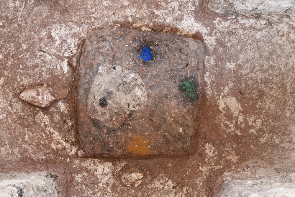 Un cuadrado de piedra con una mancha azul en la parte superior, verde a la derecha, amarilla en la parte inferior y una concha de color crema a la izquierda.
