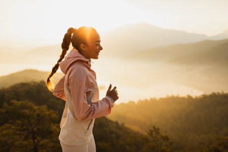 Happy young woman running outdoors with mountain view at sunset or sunrise