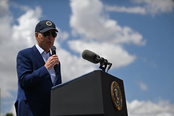 US President Joe Biden speaking outdoors with microphone in front of blue skies.