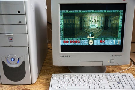 A vintage desktop computer from the 1990s on a table with the game DOOM seen on the display